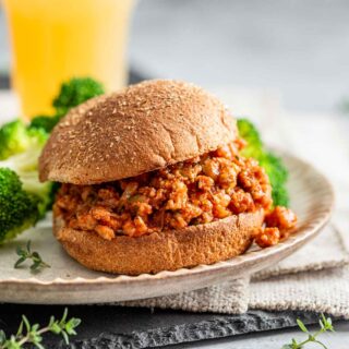 ground turkey sloppy joe meat on a bun with lettuce and an orange beverage in the background