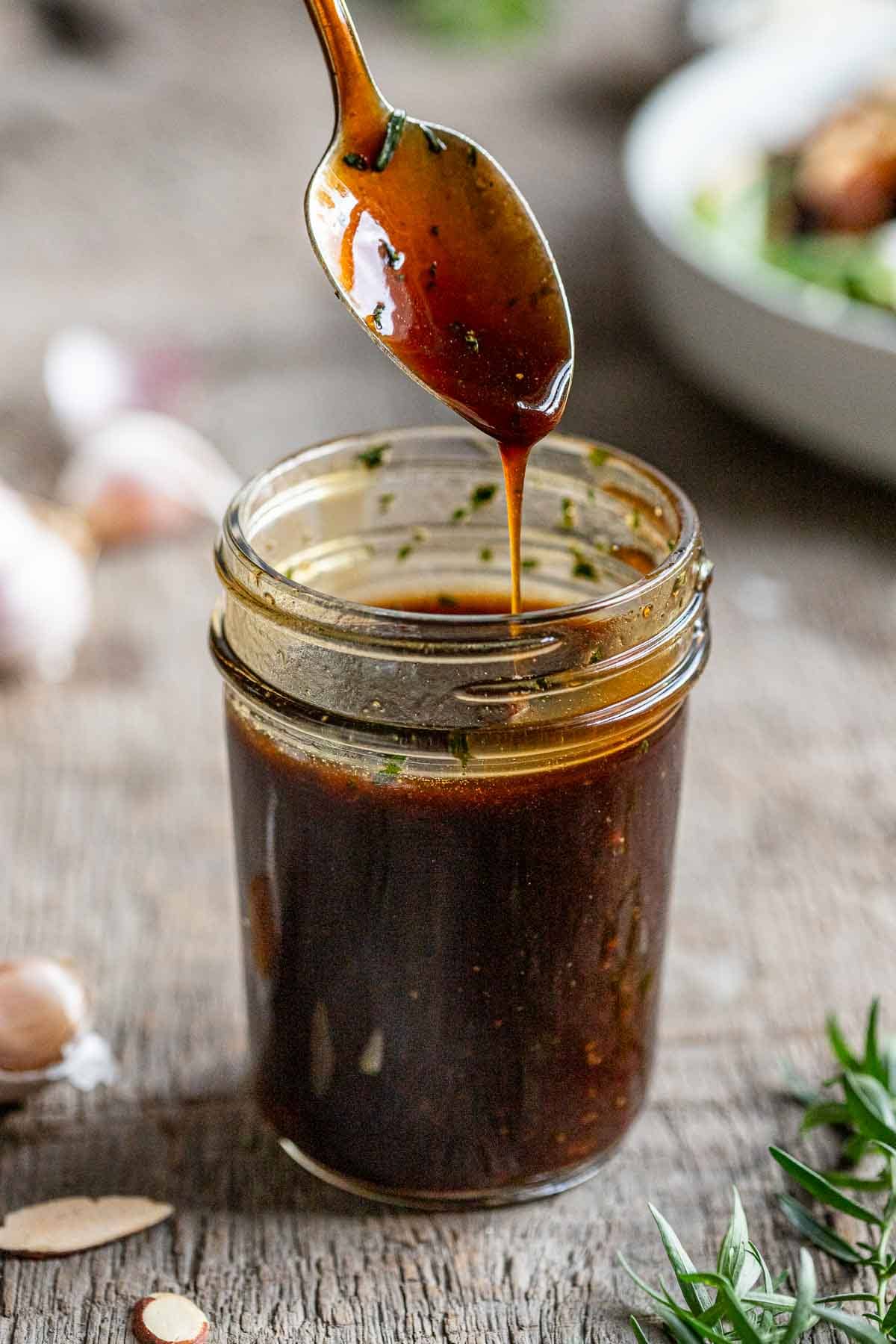 Maple balsamic salad dressing being dripped off the a spoon into a mason jar