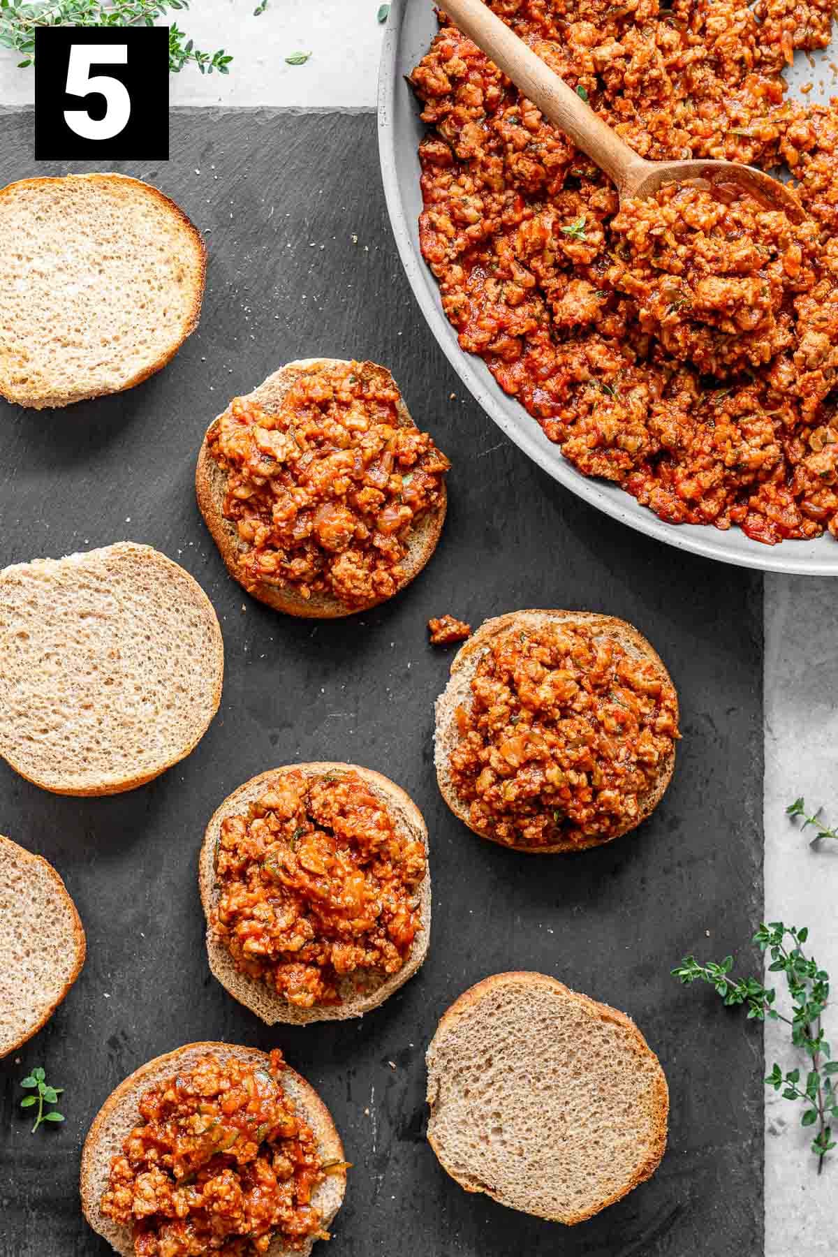 in the top right corner is a bowl full of ground turkey sloppy jane mix and filling the rest of the photo are several bun halves with some of them topped with the mixture