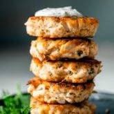 A stack of Lemon Caper Salmon Cakes on a black plate with a sprig of dill