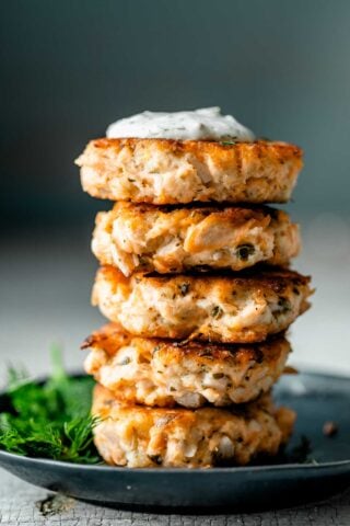 A stack of Lemon Caper Salmon Cakes on a black plate with a sprig of dill