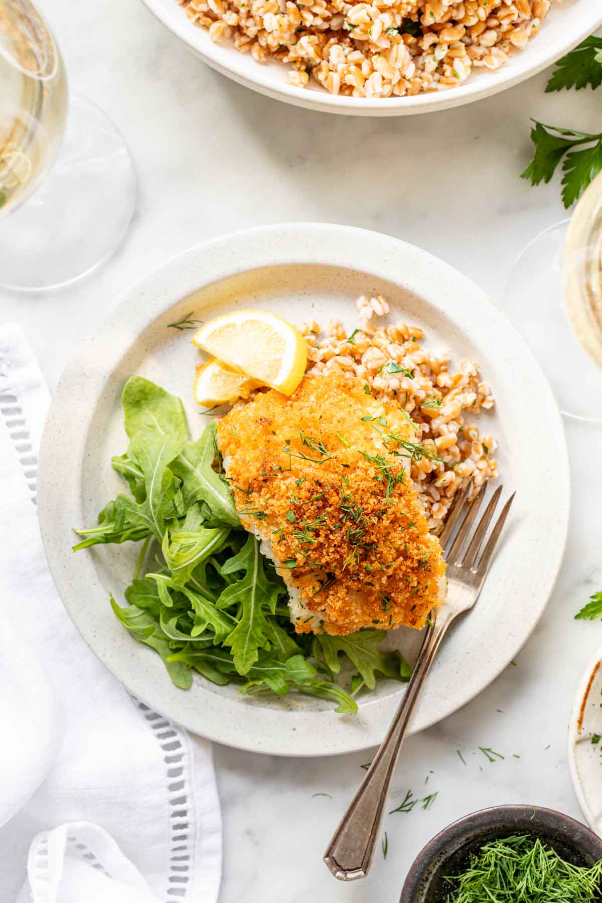 overhead photo of panko crusted cod fish on circular white plate with fork and simple green salad