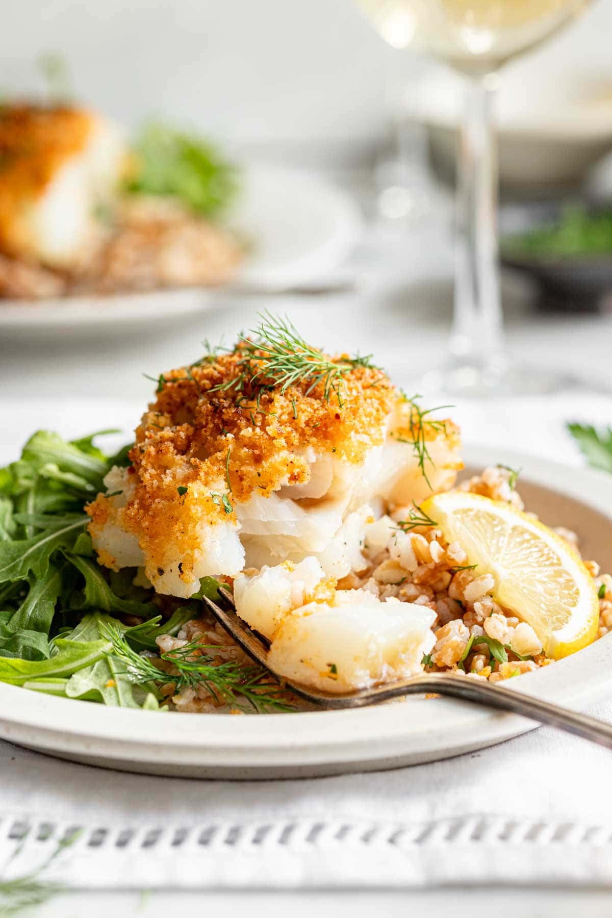 side view of sliced baked cod recipe with panko on circular white plate with a fork