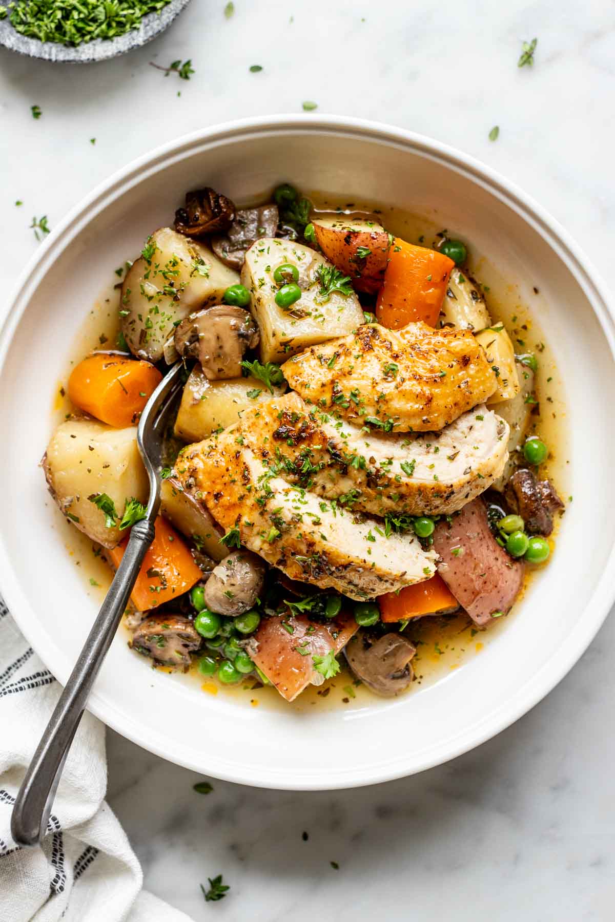 overhead photo of the roast chicken and vegetables in a white bowl with a fork sticking out the side