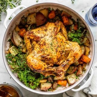 an overhead photo of a pot roast chicken in a dutch oven over vegetables