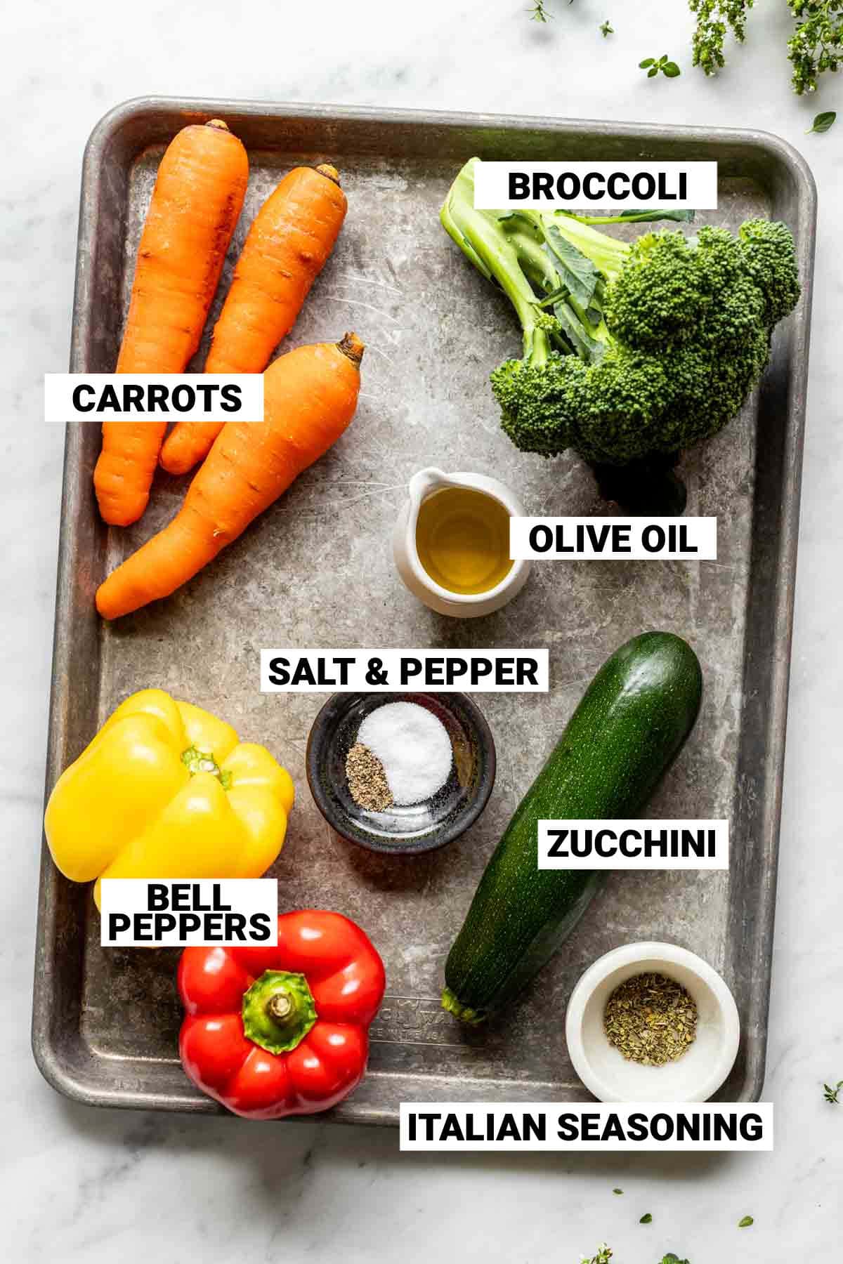 zucchini, salt and pepper, italian seasoning, yellow and red bell peppers, carrots, olive oil, and broccoli laid out on a silver sheet pan