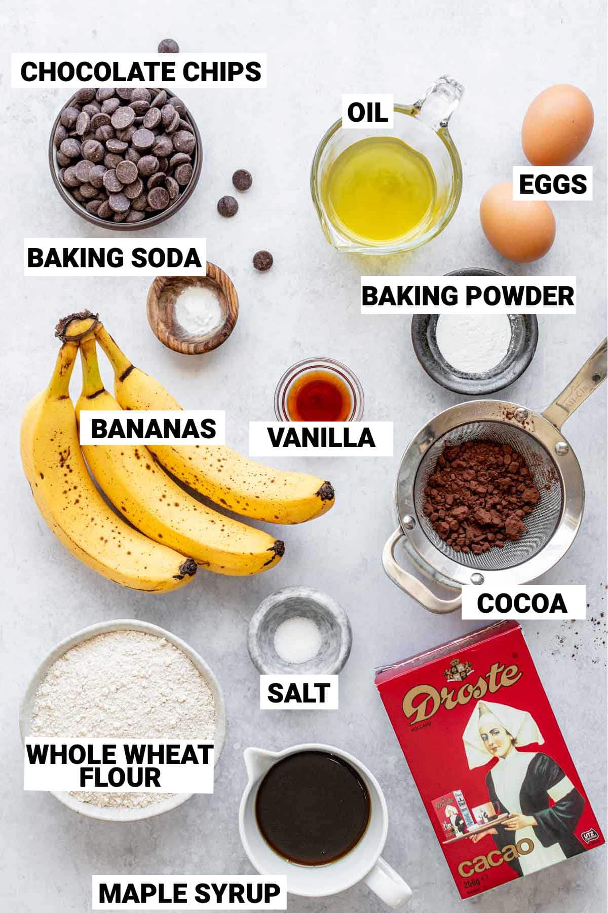 chocolate chips, oil, eggs, baking soda, baking powder, vanilla, banana, salt, cocoa, maple syrup, and whole wheat flour set out to make whole wheat chocolate banana bread