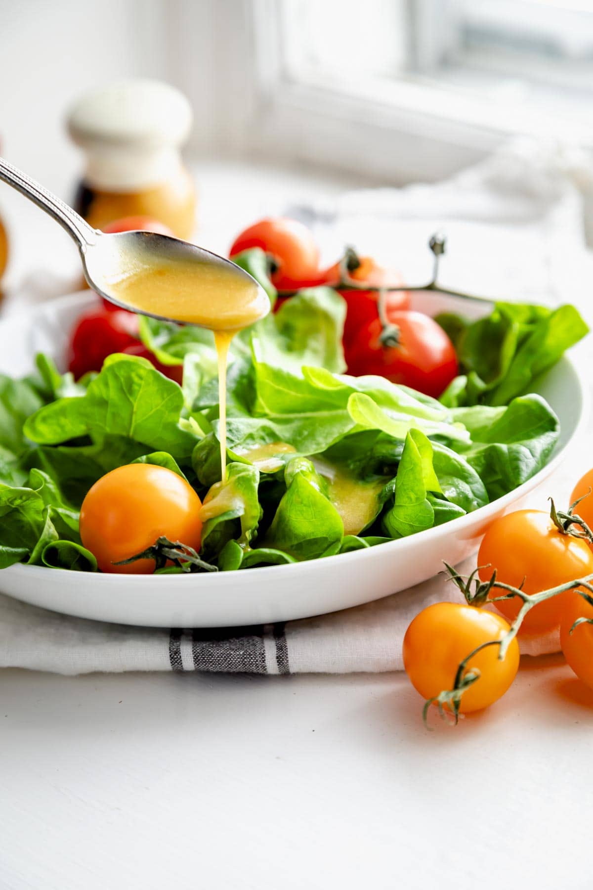 orange miso vinaigrette being spooned over a bed of greens with fresh grape tomatoes