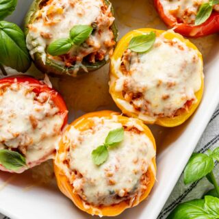 Healthy stuffed peppers with cheese on top and basil leaves garnishing from overhead in a white casserole dish
