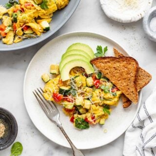 a white plate with scrambled eggs, toast and avocado