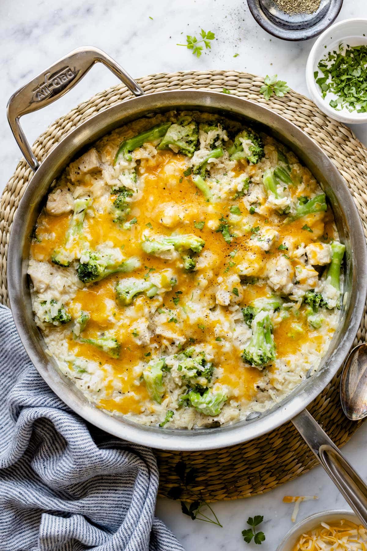 the skillet resting on a woven placemat with the chicken rice recipe inside it with broccoli and melted cheese