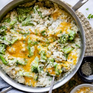 a stainless saute pan with chicken, rice and broccoli covered in melted yellow cheese