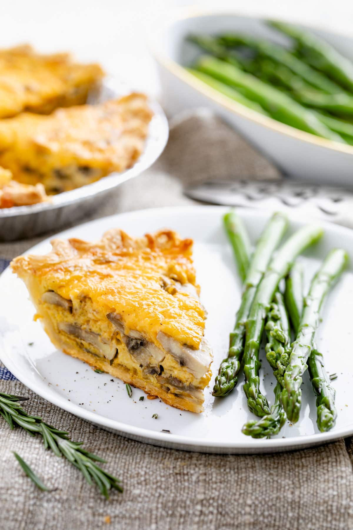 a slice of the mushroom quiche on a white plate with steamed asparagus