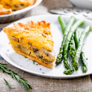 a slice of the mushroom quiche on a white plate with steamed asparagus and a shiny fork