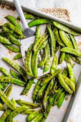 a spatula full of the snap peas on the sheet pan