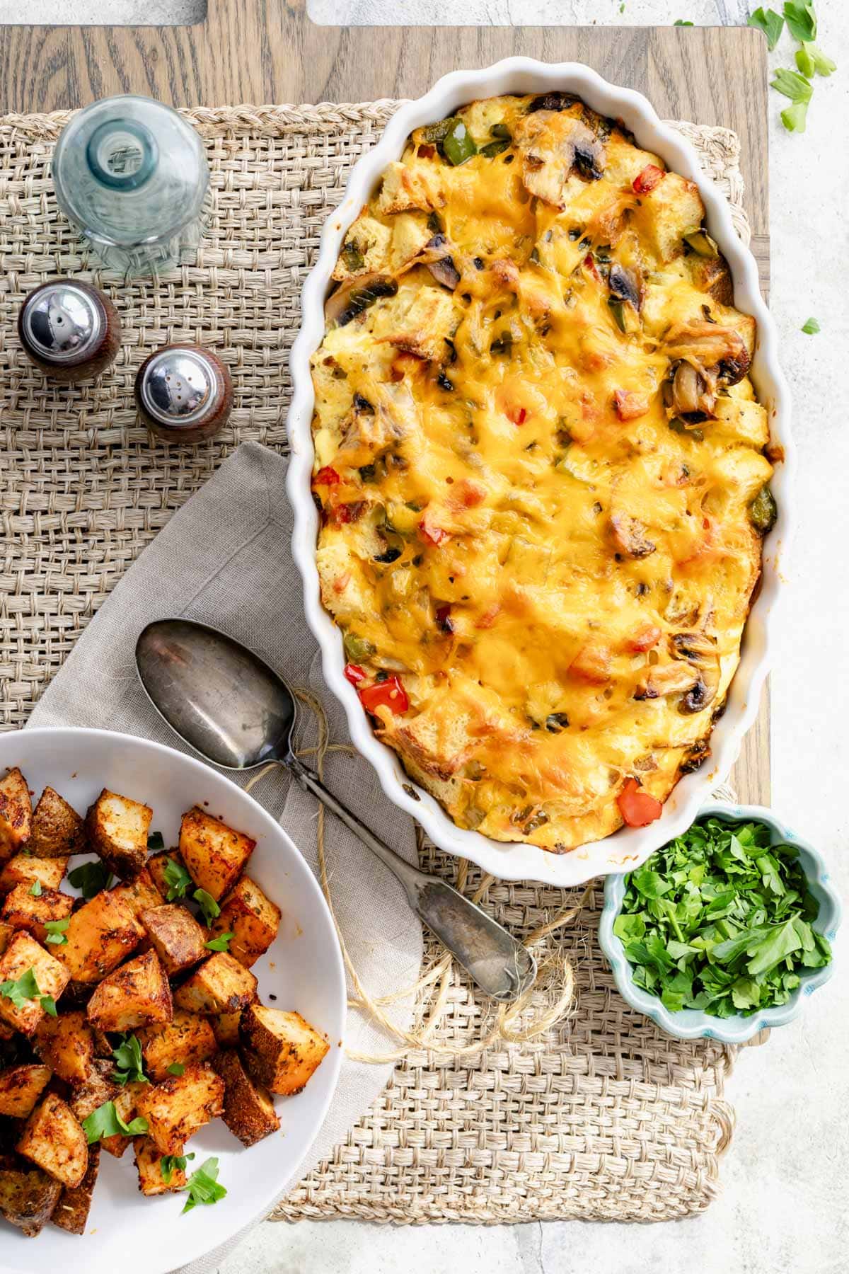 overhead of the table set with a casserole dish with the strata and a white bowl of home-fried potatoes