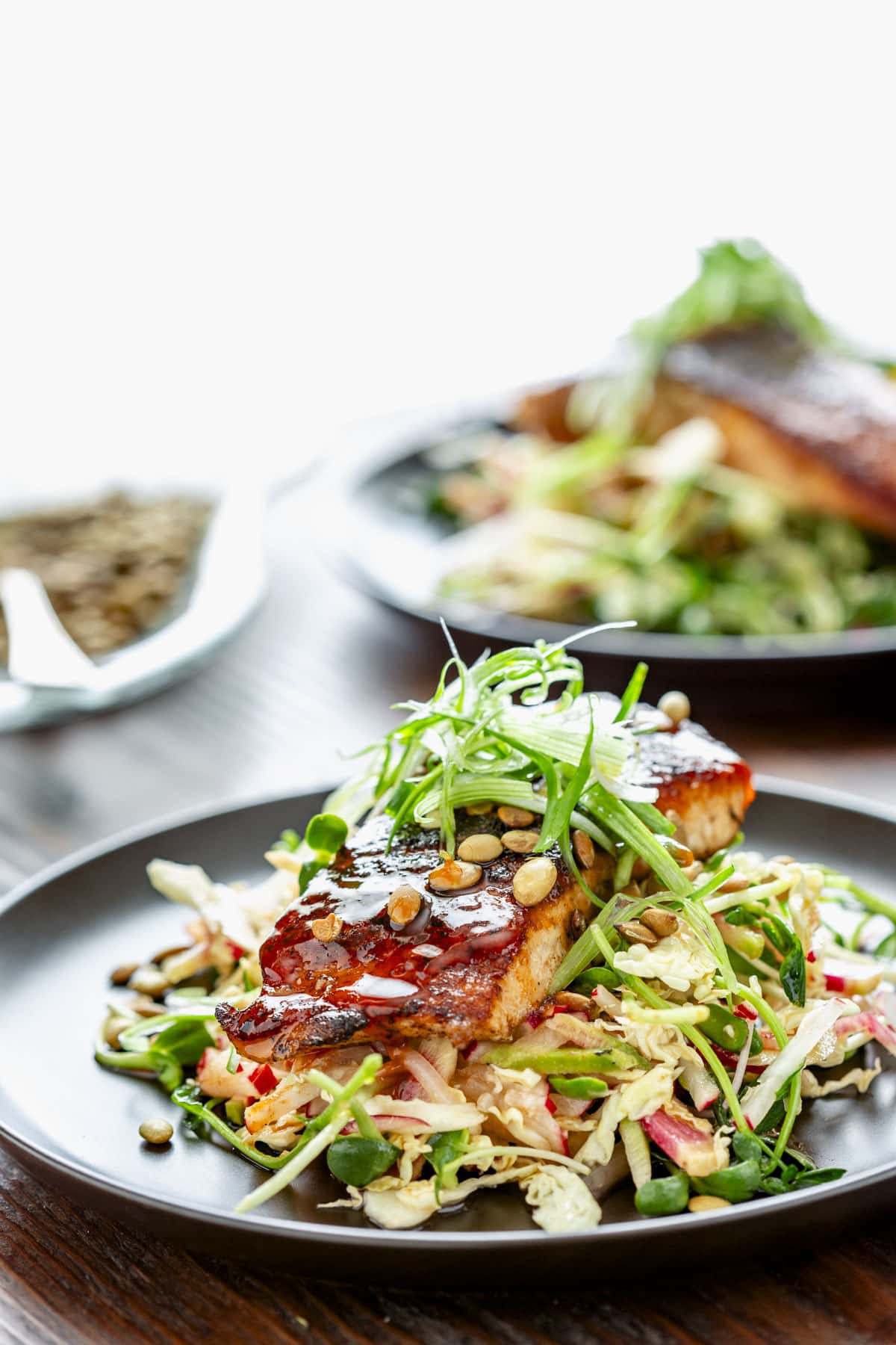 the blackened salmon on top of the shredded slaw with scallion frizzle on top on a black plate on a wooden tabletop