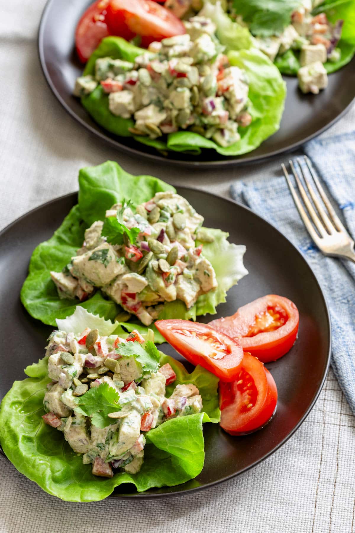 two lettuce cups with the Mexican Chicken Salad on a black plate with tomato wedges