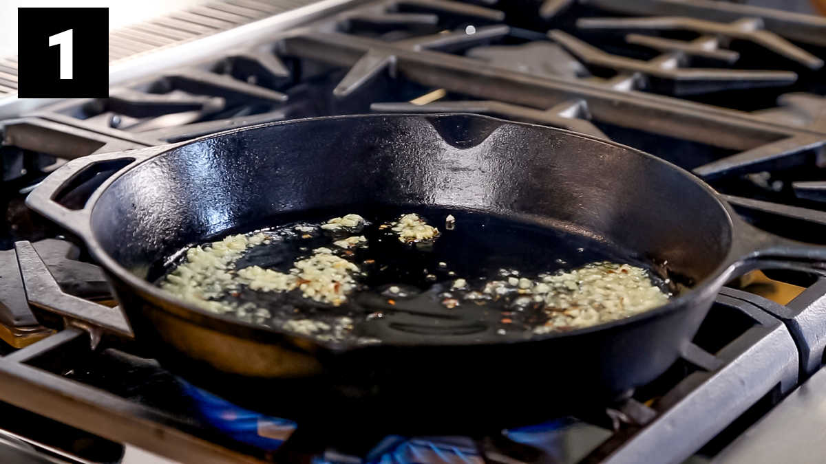 the cast iron skillet from the side with garlic sizzling in the oil