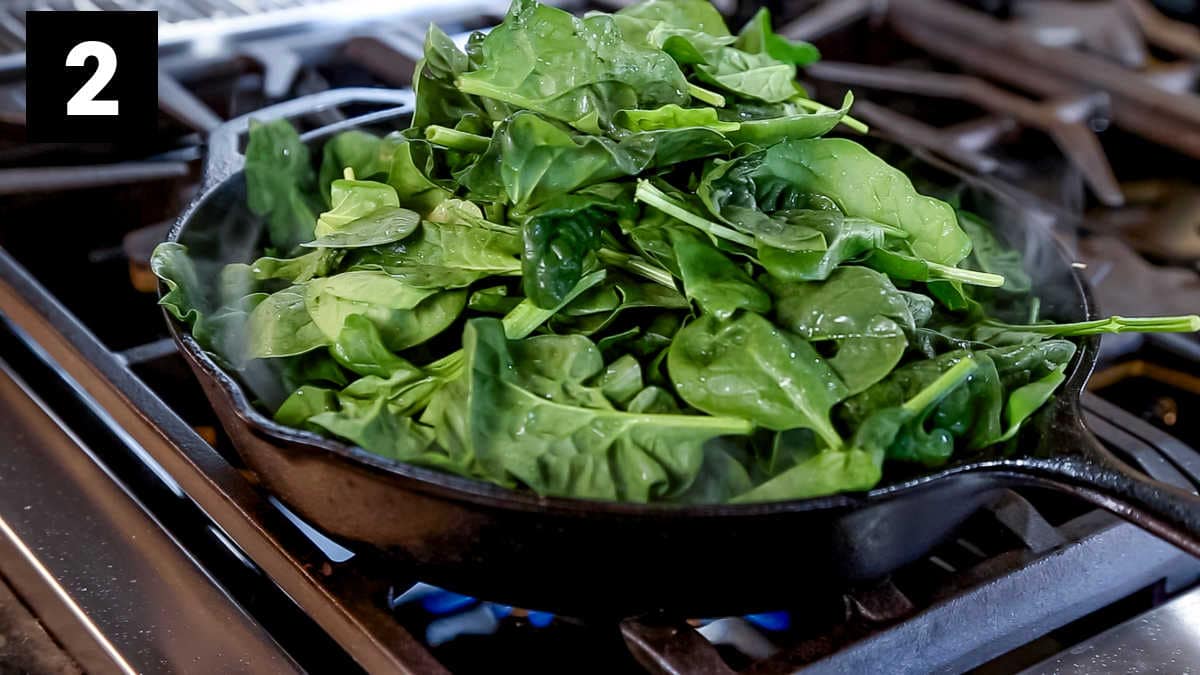 the cast iron skillet from the side with a huge pile of fresh spinach leaves in it