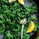 the sauteed spinach and garlic in a black cast iron skillet with fresh lemon wedges