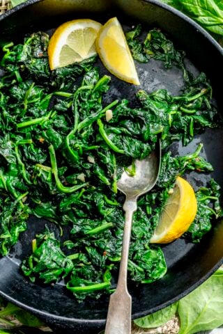 the sauteed spinach and garlic in a black cast iron skillet with fresh lemon wedges