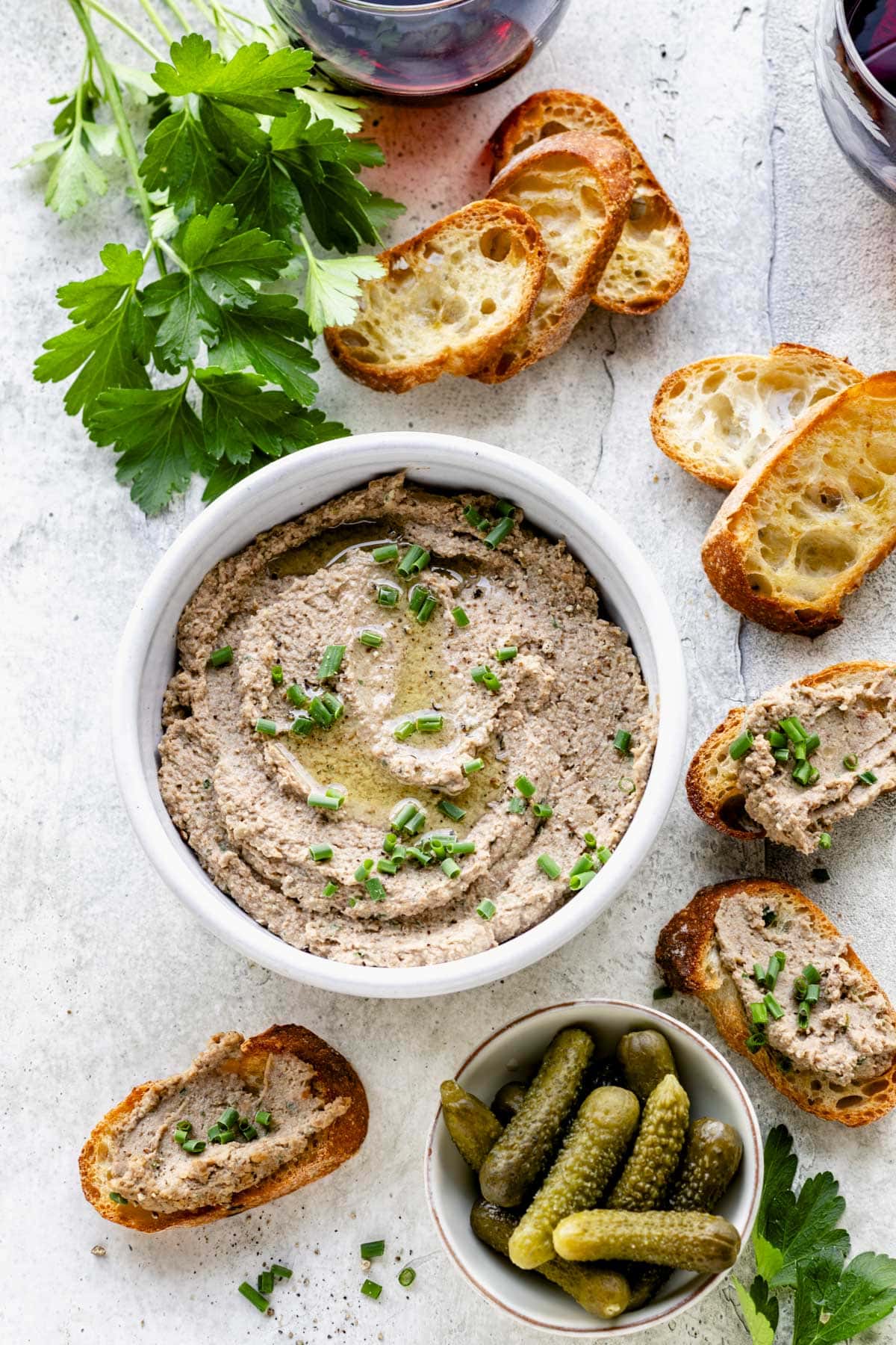 a white crock with vegan pate with a little oil and chives on top, crostini on the side