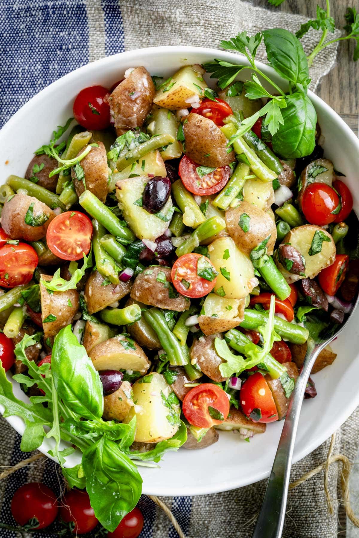 a close up of the potato salad with green beans in a white bowl from overhead
