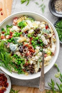 pasta salad with veggies and creamy dressing in a white bowl with a serving spoon in it
