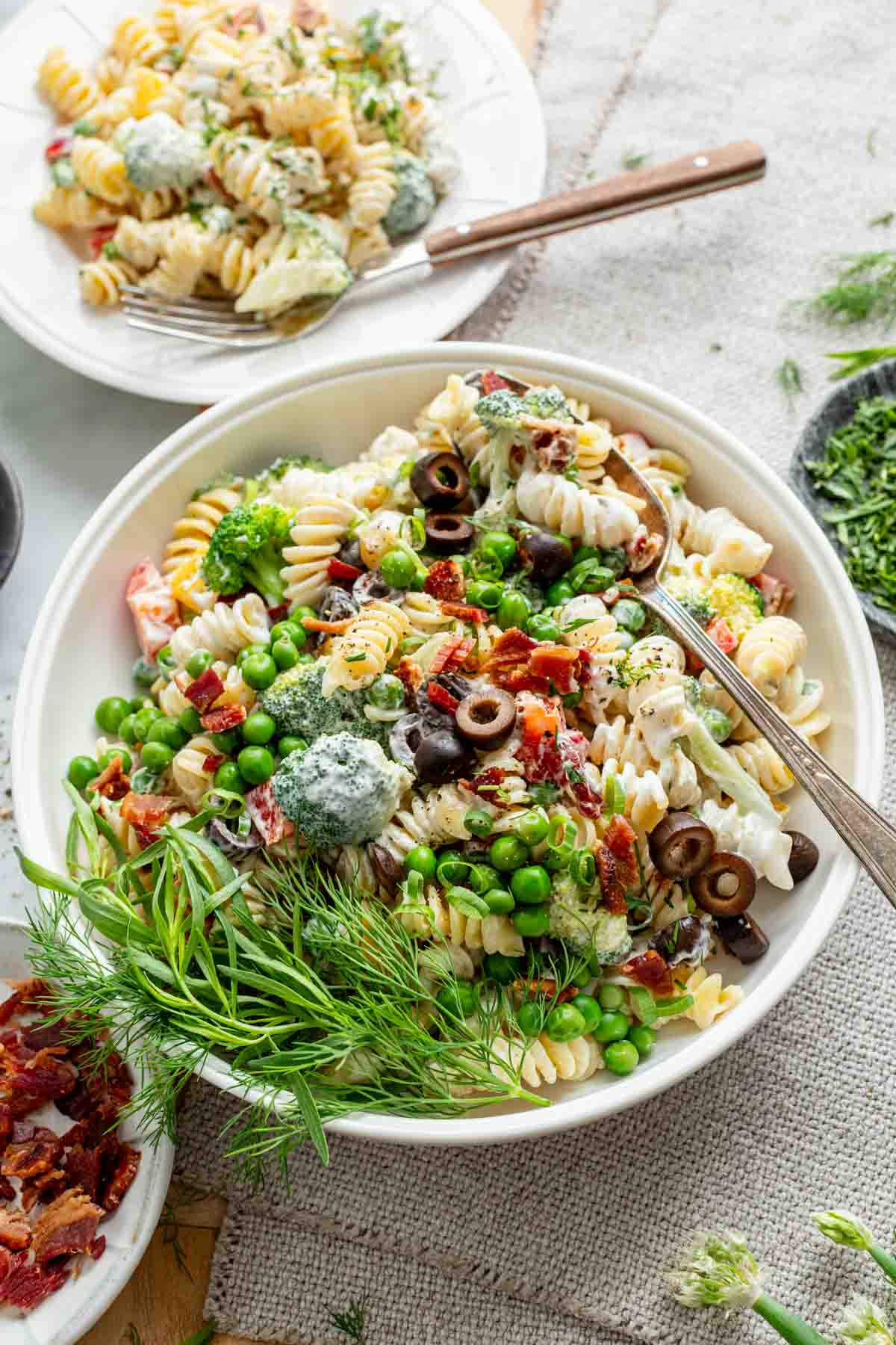 the pasta salad in a white bowl from overhead with a serving in a bowl in the background