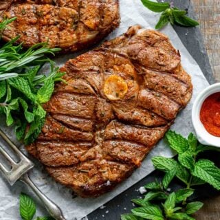 a grilled lamb steak surrounded by greens and a dipping sauce