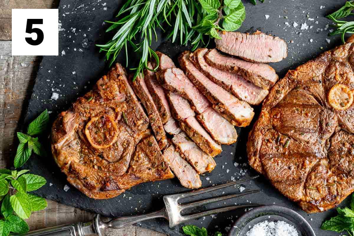 the lamb steaks on a charcoal grey cutting board with one half-sliced into strips