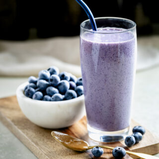 peanut butter blueberry smoothie in glass cup with bowl of fresh blueberries next to the drink