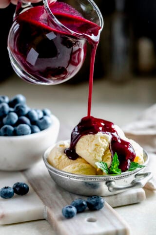 blueberry coulis being poured over a bowl of vanilla ice cream