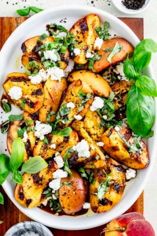 grilled peach salad on a platter with basil leaves and chevre on top
