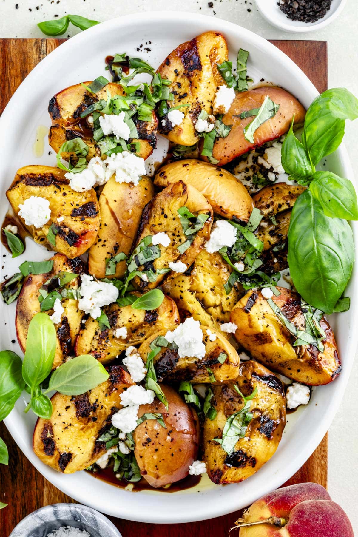 grilled peach salad on a platter with basil leaves and chevre on top