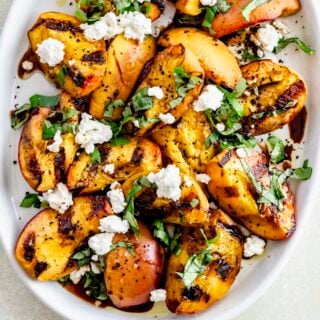 grilled peach salad on a white platter with basil on top