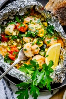 a foil packet full of shrimp, summer vegetables, and parsley and lemon garnish