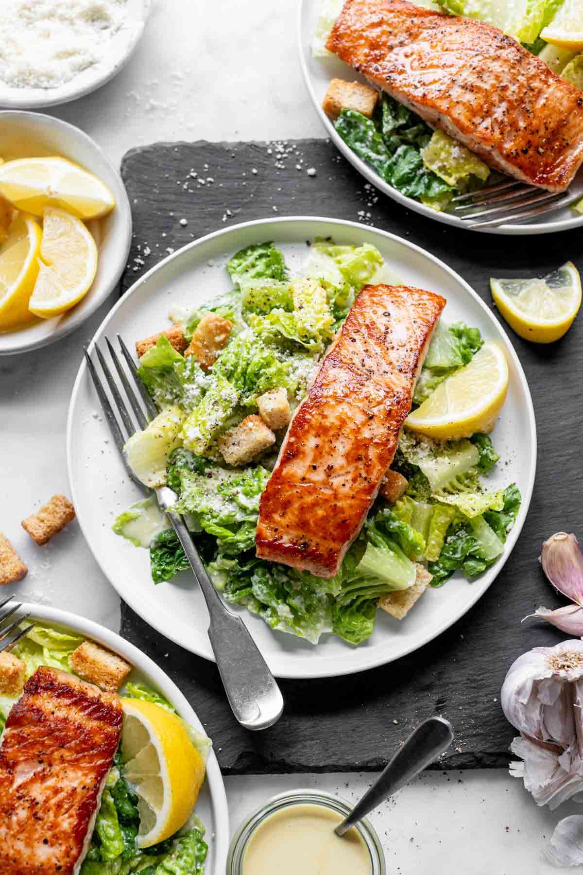 the salmon caesar on three plates with a slate board and white table