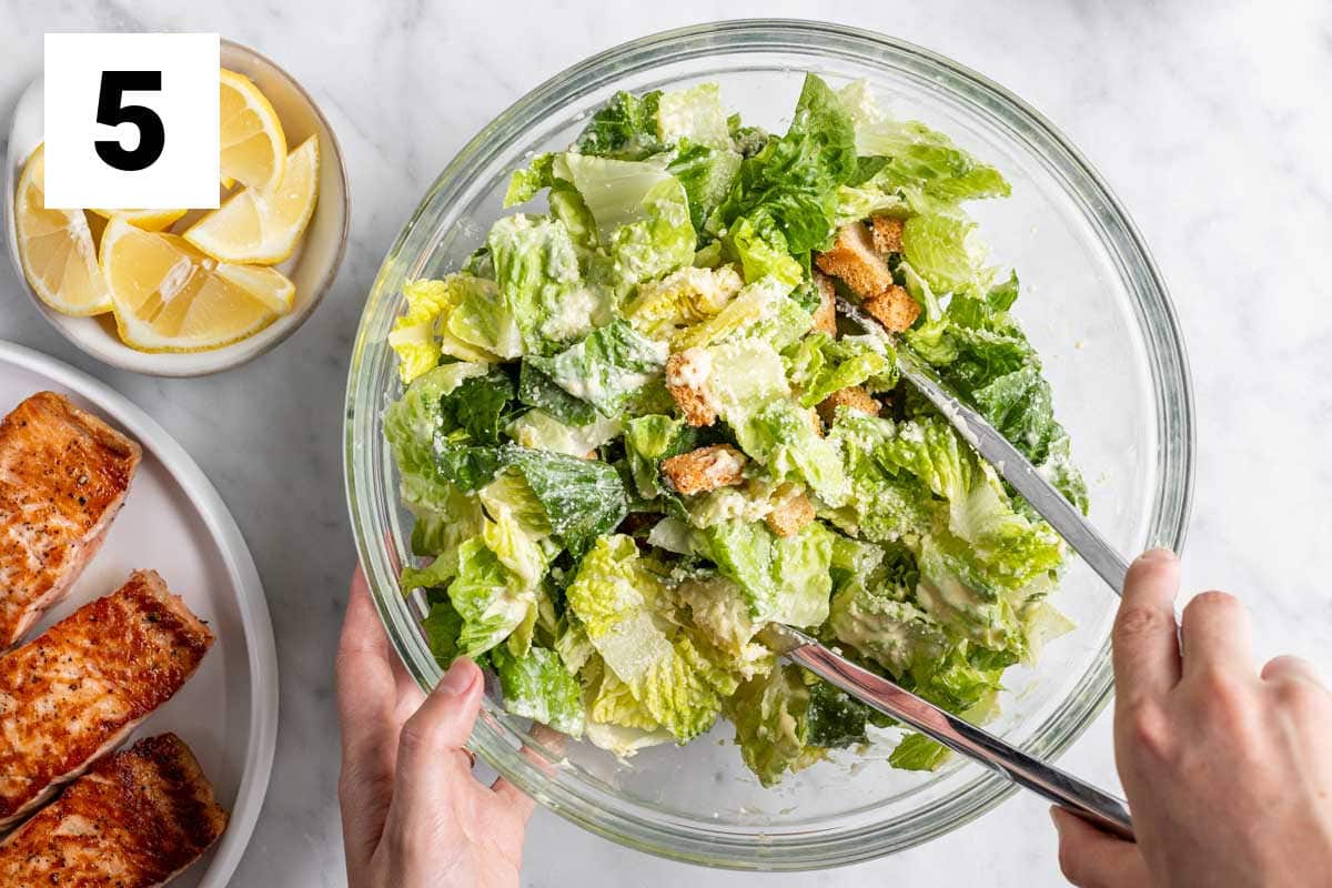 tossing the caesar dressing with the romaine lettuce in the bowl with tongs