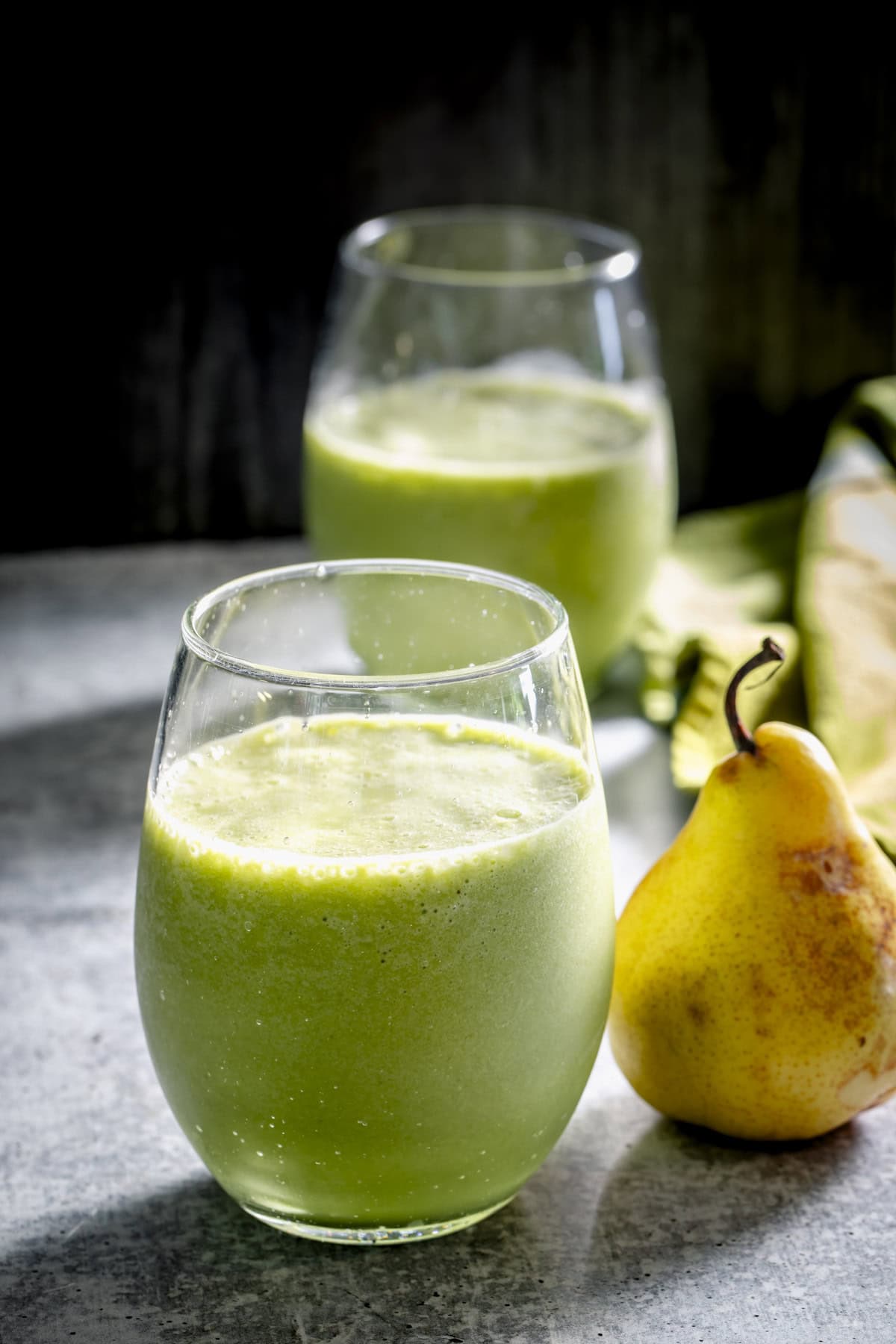 the pear smoothie with one in the background and a ripe yellow pear next to it