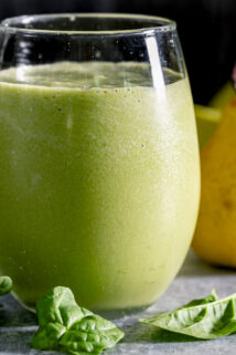 the green smoothie in a tumbler with a yellow pear in the background