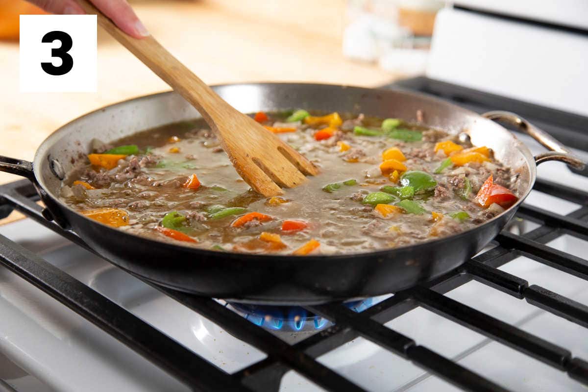 the skillet with the broth added to it and a wooden spatula stirring the mixture