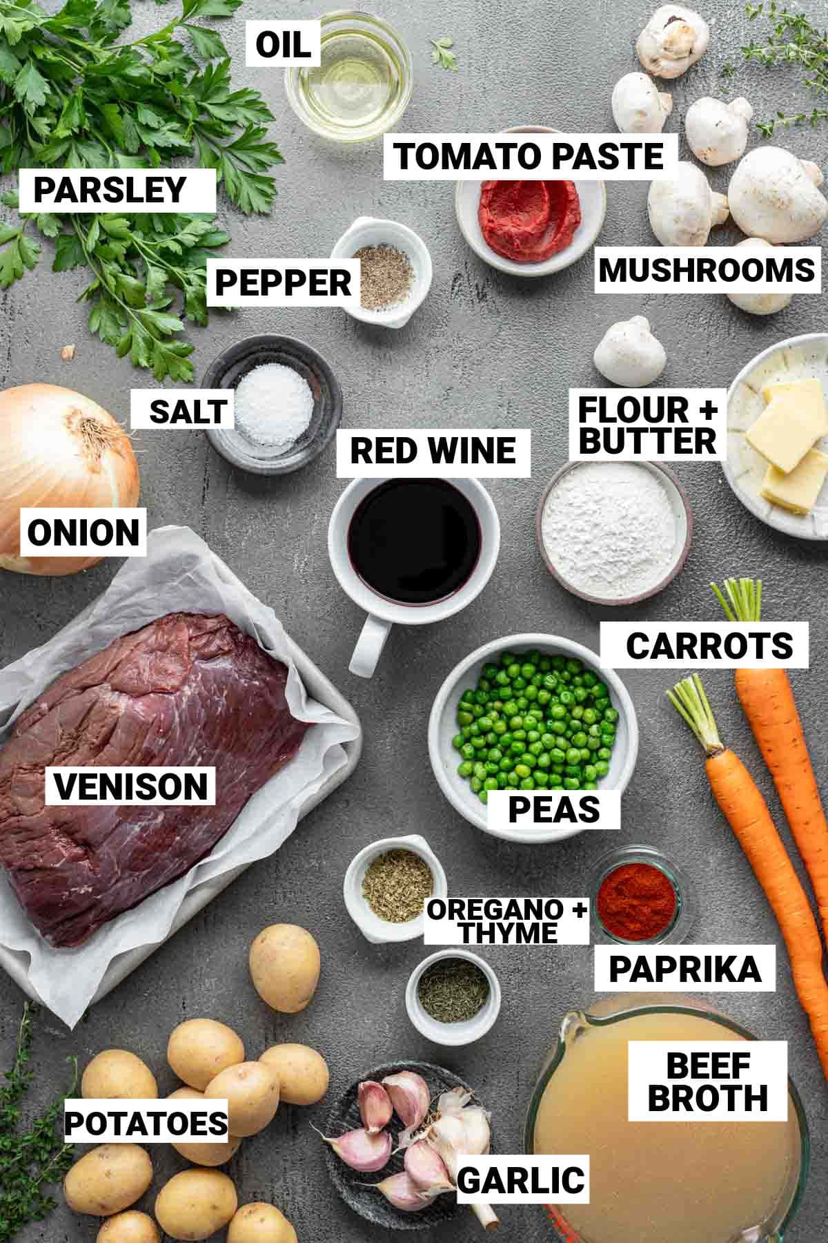 the ingredients for the venison stew on a gray tabletop with text overlay labels on each item