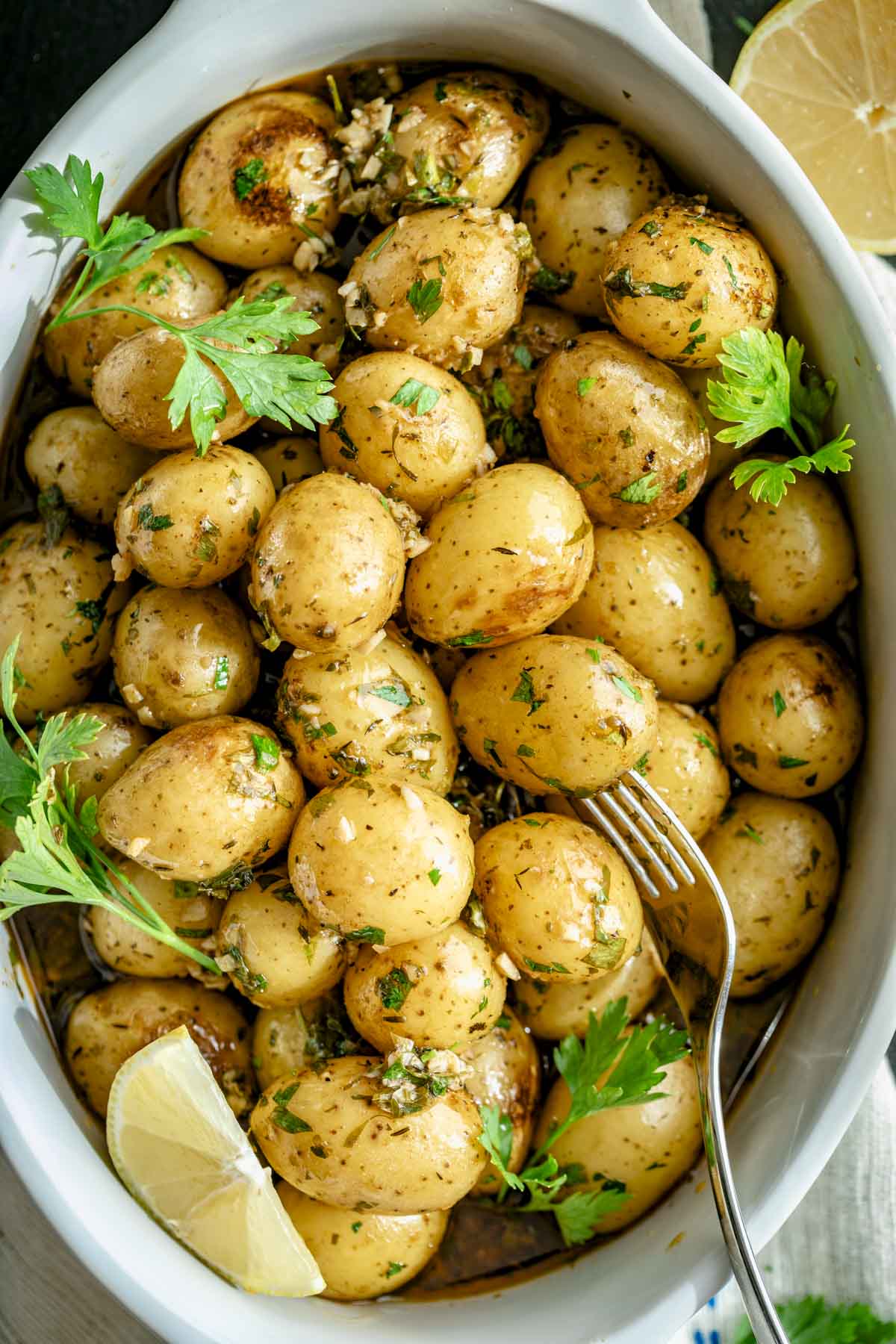 the Greek-Style Potatoes recipe in a ceramic dish with parsley sprigs and lemon wedges