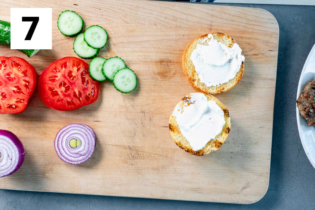 toasted buns with labneh on them and sliced cucumbers, onions, and tomatoes to the left