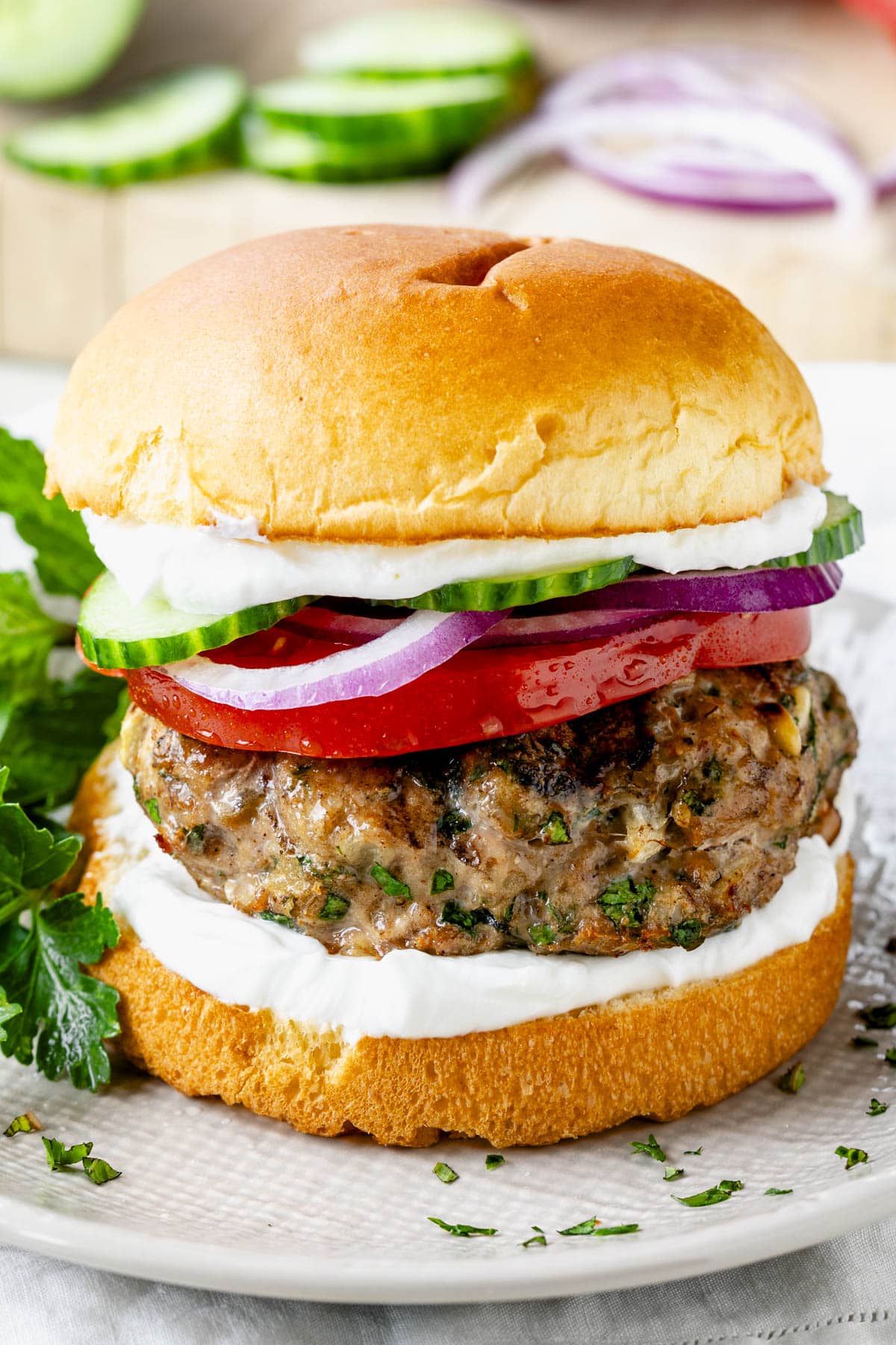 a turkey burger on a bun with red onion, cucumbers, and greek yogurt