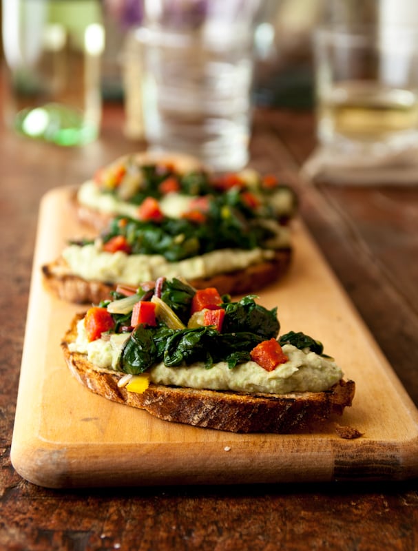 bean and green bruscetta sitting on top of a wooden cutting board