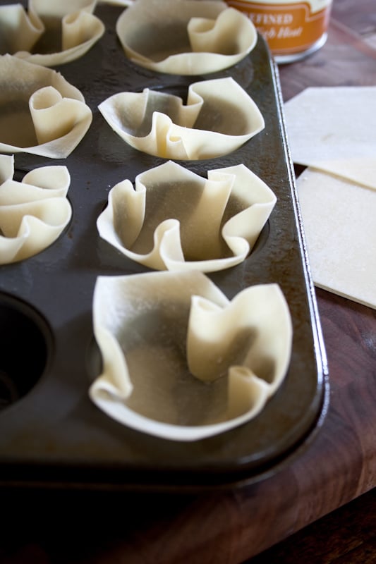 A mini muffin tin with uncooked wonton wrappers stuffed into each muffin welll before baking