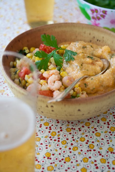 shrimp and corn with cheese grits shrimp and corn with cheese grits in a bowl with a spoon and a glass of beer in front and another glass of beer and a bowl of parsley in the background
